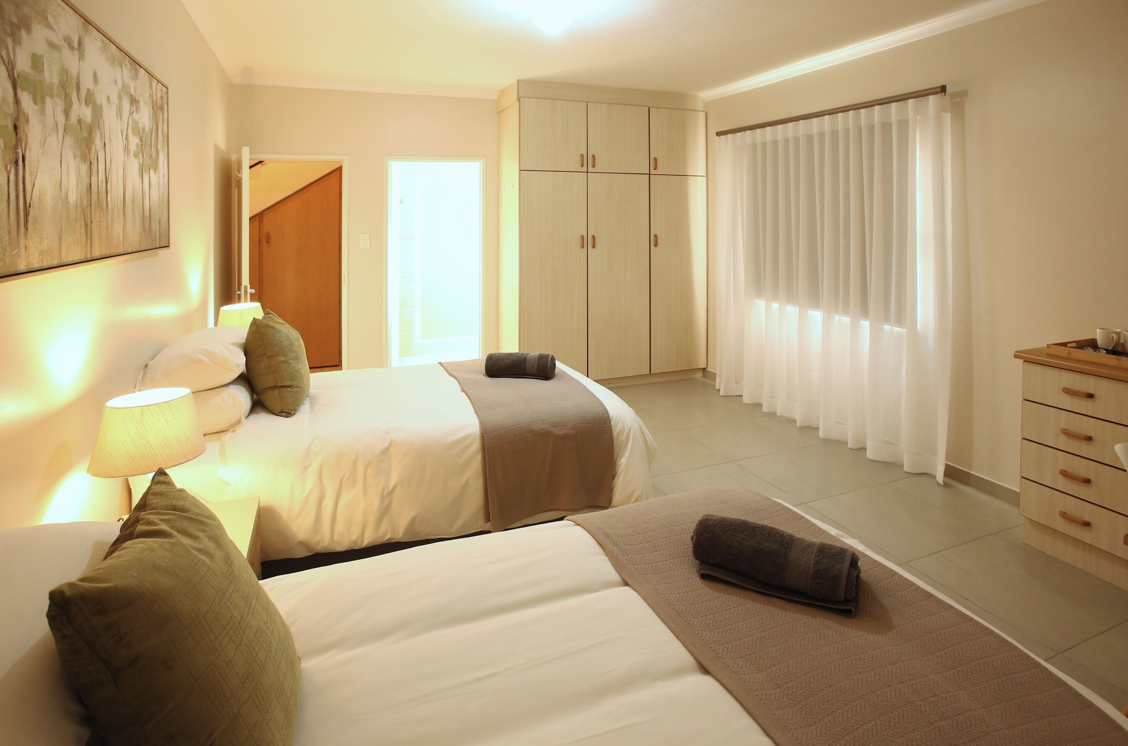 Habitación de hotel con dos camas, un armario, un escritorio y un amplio ventanal con cortinas.