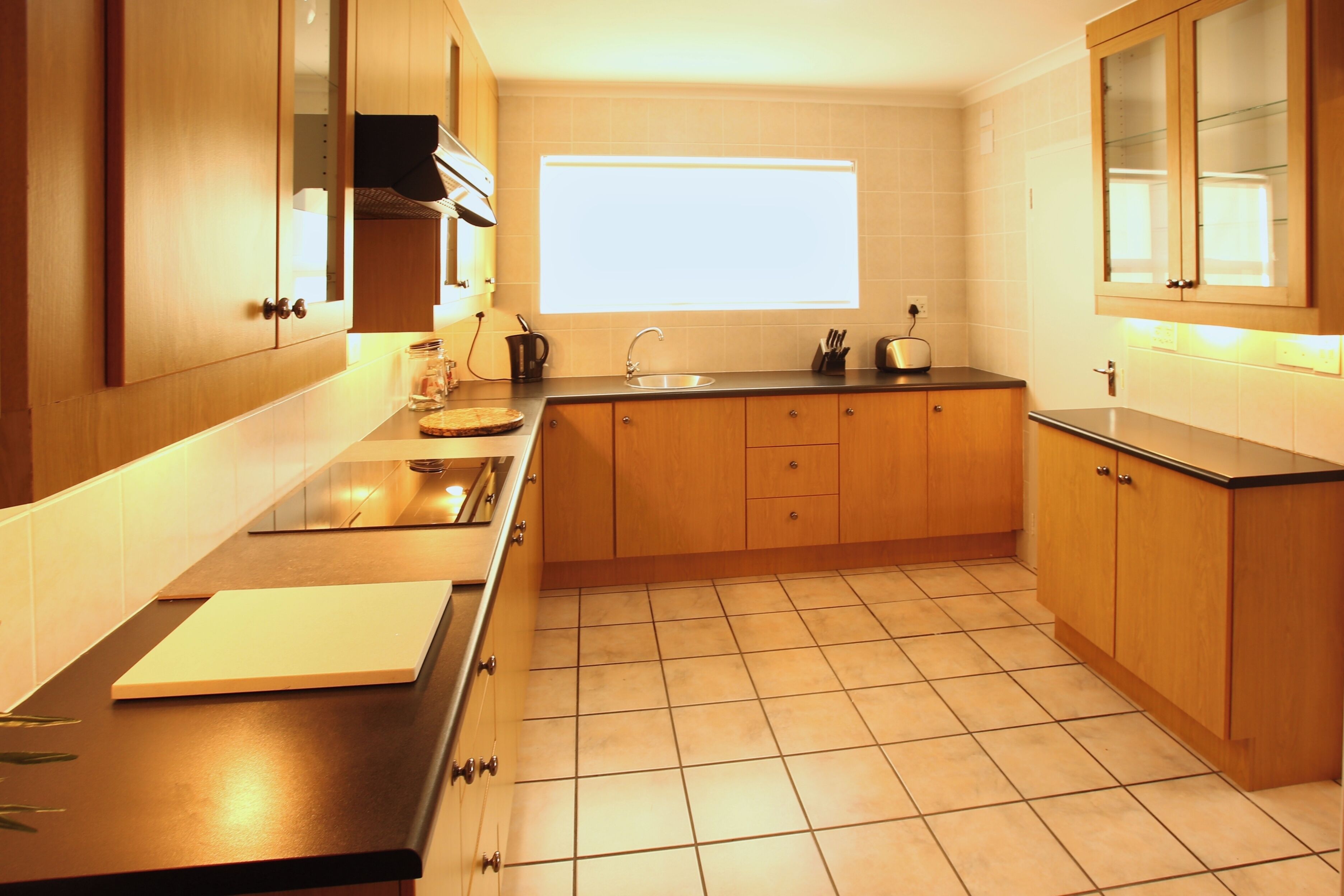A kitchen with wooden cabinets, a black countertop, a window, and a tiled floor.