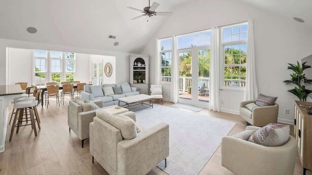 A spacious living area with a high ceiling, a ceiling fan, and large windows offering a view of the outdoors. - 723 Seahorse Road (Fripp Island)