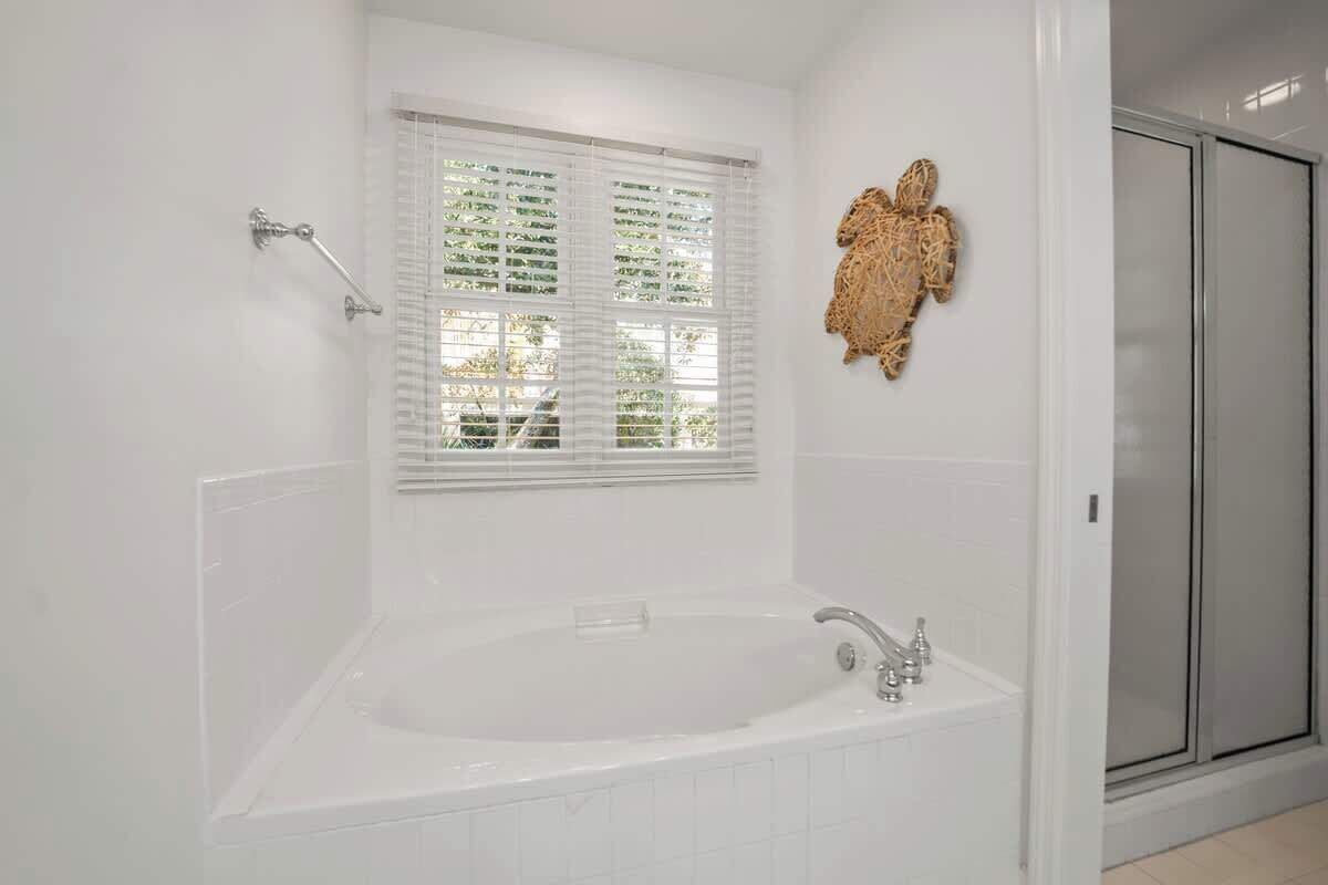 Un baño con una bañera grande, una ventana con persianas y una cabina de ducha.