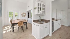 A modern kitchen with white cabinetry, a granite countertop, and a dining area with a wooden table and wicker chairs. - 723 Seahorse Road (Fripp Island)