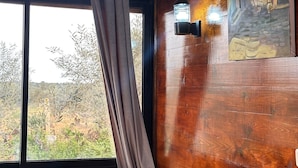 A wooden interior with a bed, checkered pillows, a painting, and a window with curtains. - La Cascina (Sidi Bou Ali)