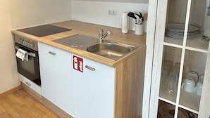 A compact kitchen with a built-in oven, a sink, and a cabinet with glass doors. - Modern Flat | washing machine, underfloor heating, rain shower (karlsruhe)