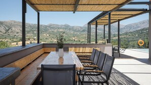 An outdoor dining area with a long table and chairs, a potted plant, and a view of mountains. - Kourtaliotis Villa Crete (Agios Vasileios)