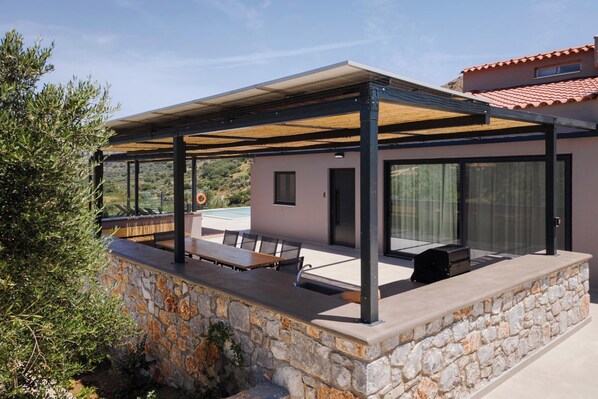 A covered outdoor seating area with stone walls and a pool in the background.