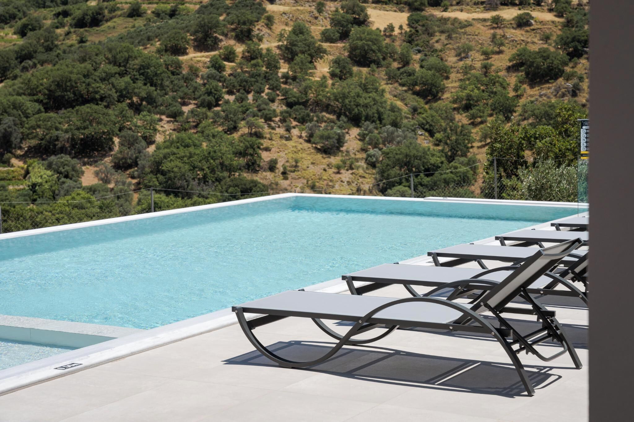 Uma piscina infinita no terraço com espreguiçadeiras e vista para uma paisagem montanhosa.
