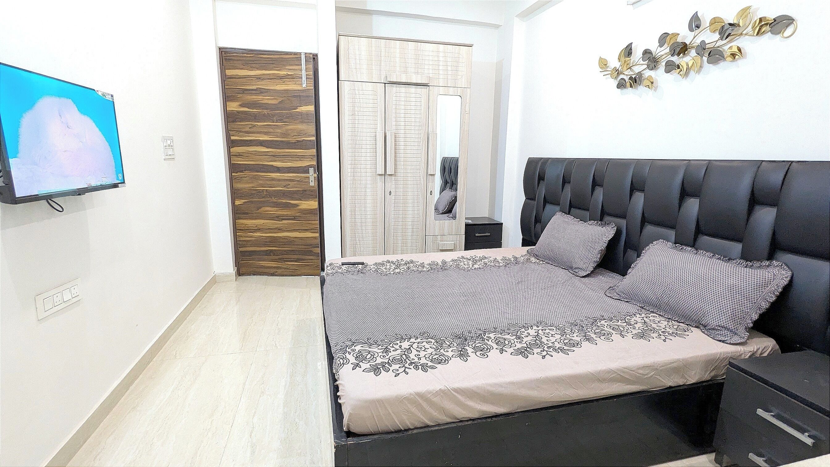 A bedroom with a bed, a nightstand, a TV, a wardrobe, and a mirror.