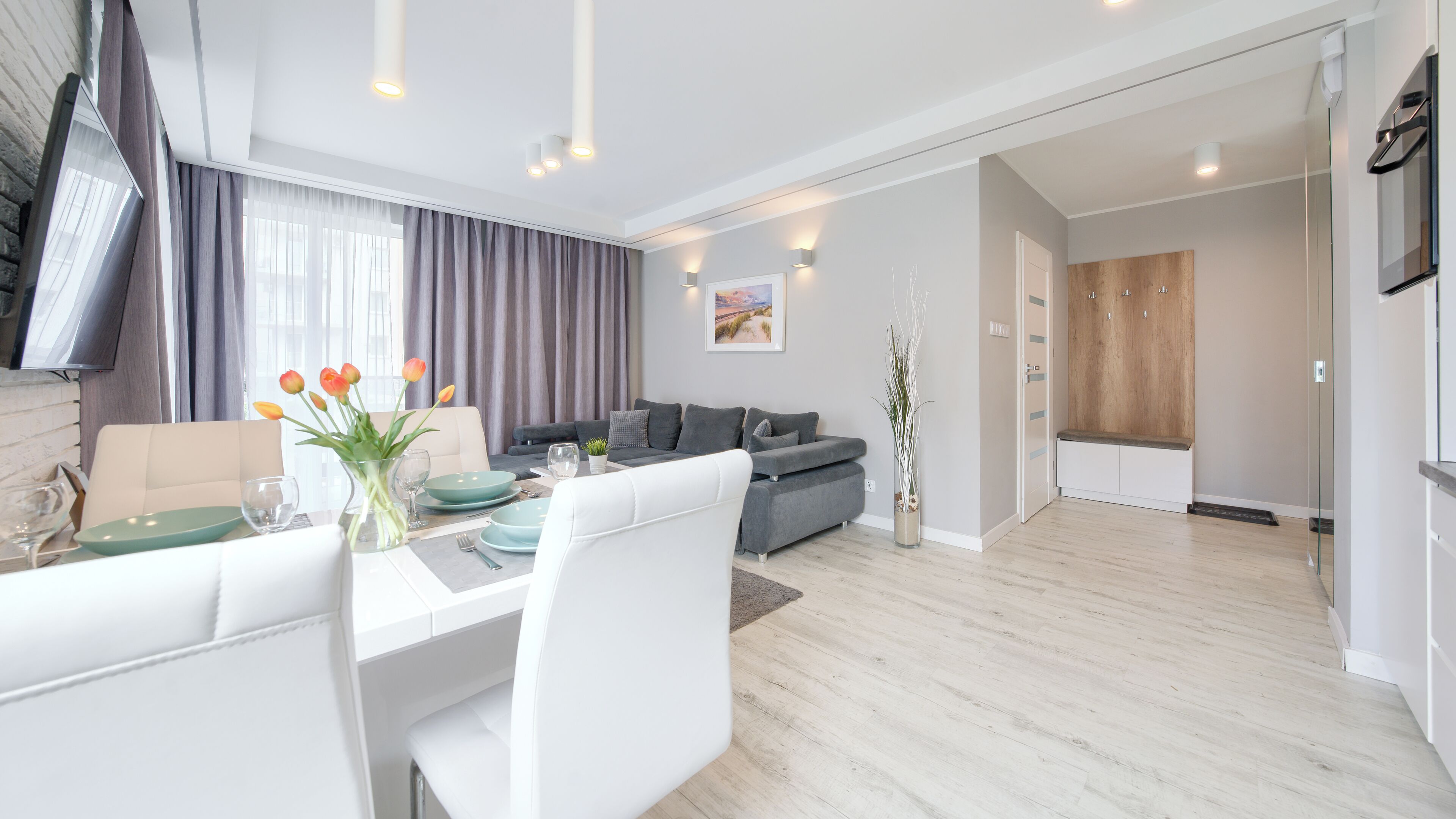 Un salon moderne avec un coin repas, des canapés gris et une table à manger blanche.