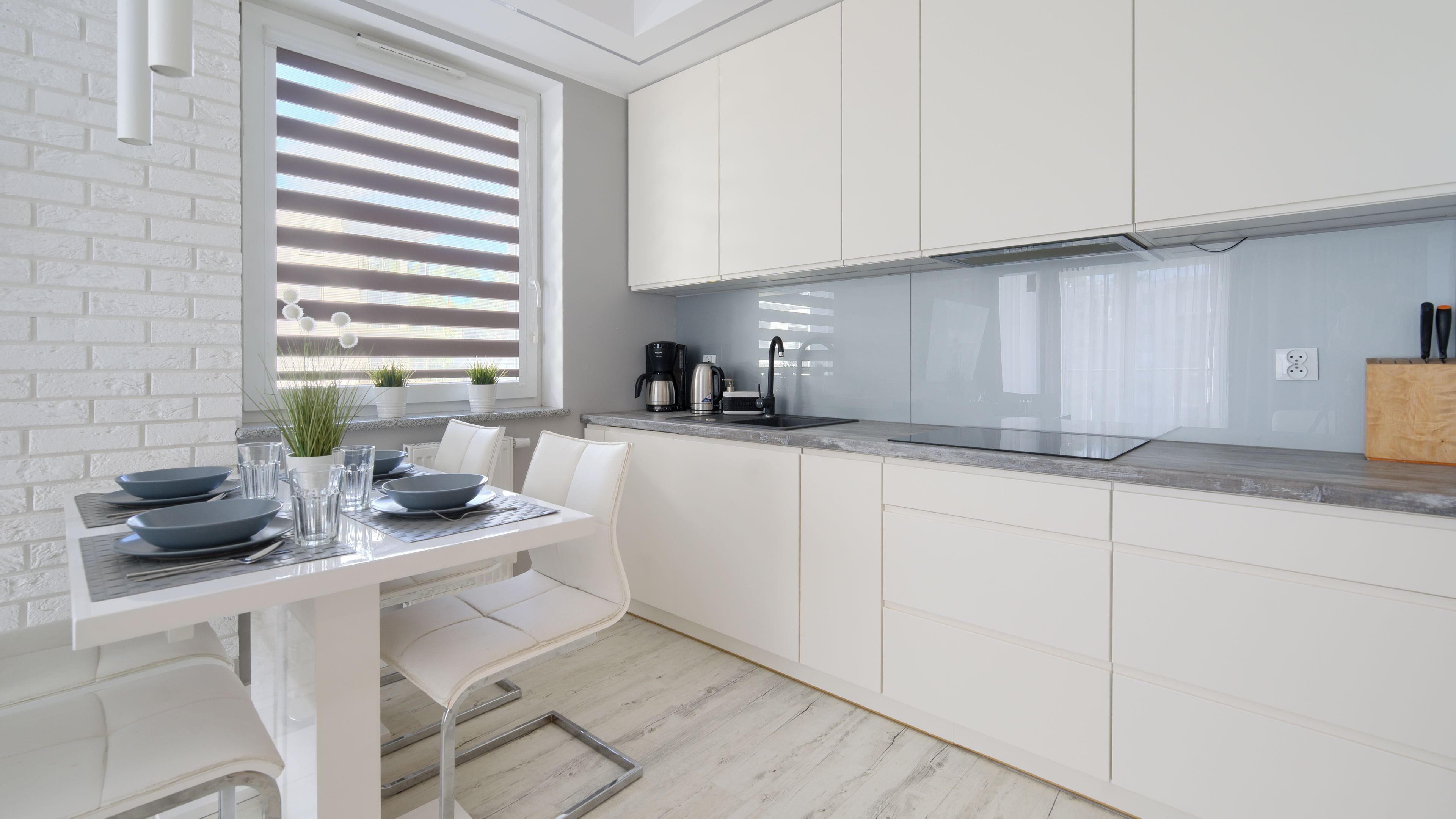 A modern kitchen with white cabinetry, a built-in stove, and a dining area with a table set for two.