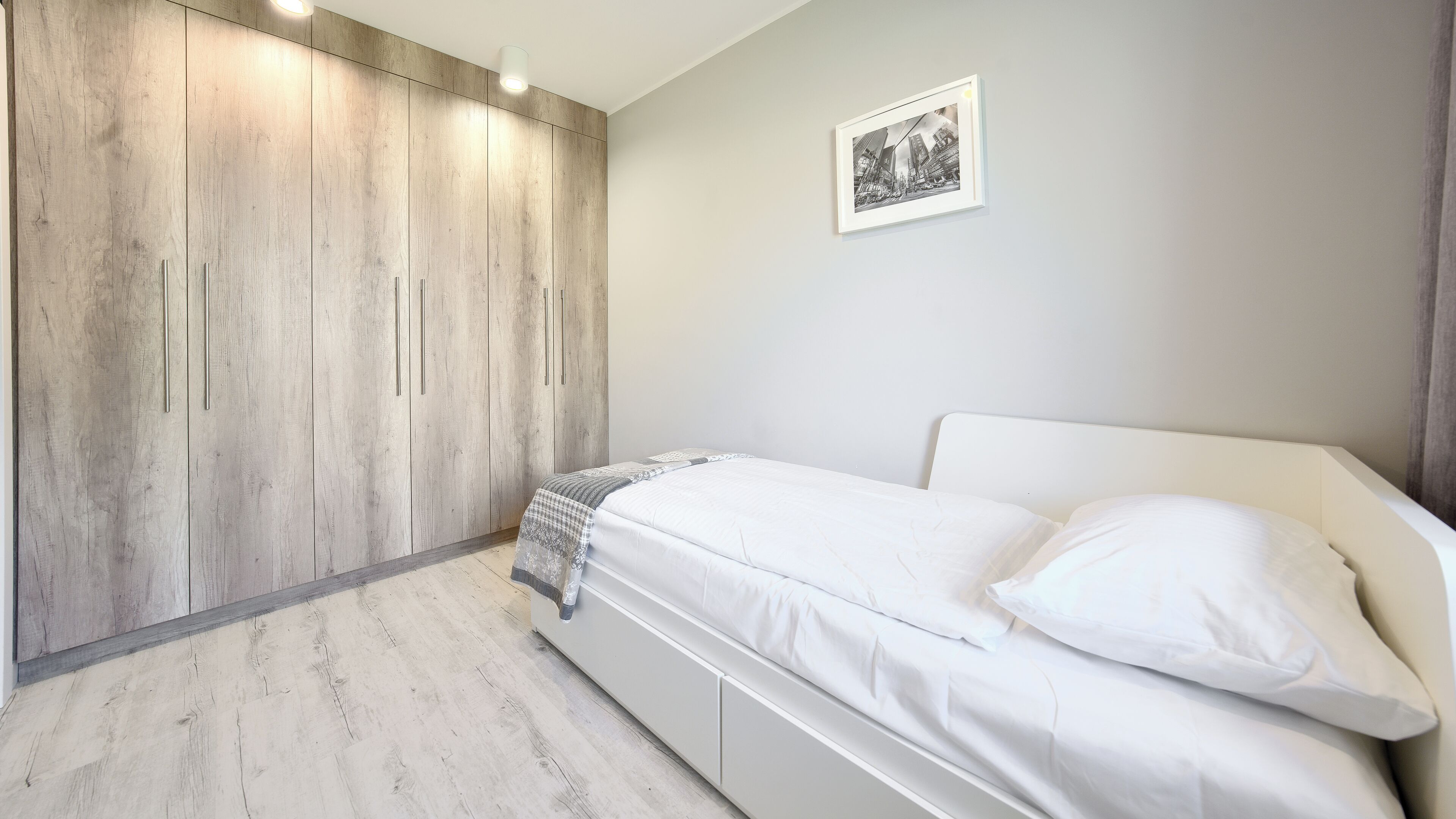 A bedroom with a bed, a wardrobe, and a framed picture on the wall.