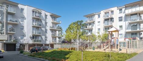 A modern apartment building with multiple balconies, a playground, and a parking area.