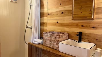 A bathroom with a wooden wall, a white sink with a black faucet, a woven basket, and a shower with a white curtain.