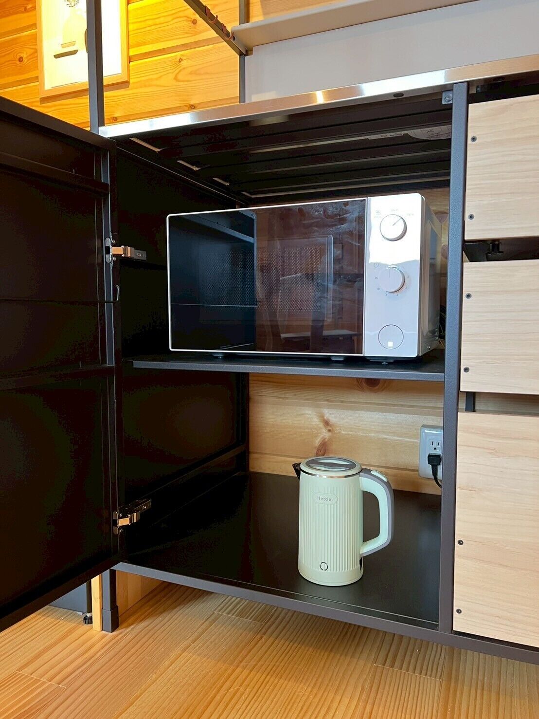 Une cuisine compacte équipée d’un four à micro-ondes, d’une bouilloire et d’une prise électrique sur le plan de travail.