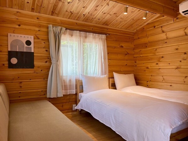 Habitació de cabana de fusta amb dos llits, una finestra amb cortines lleugeres i una obra d'art de l'estil Bauhaus a la paret.