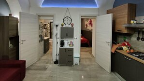 Une cuisine moderne avec un îlot central, un coin repas doté d’une table rouge et un couloir menant à une chambre.
