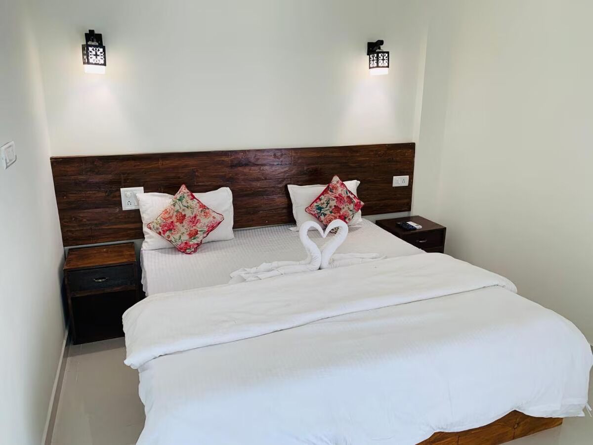 A neatly made bed with white linens and floral pillows, a wooden headboard, and bedside tables with lamps.