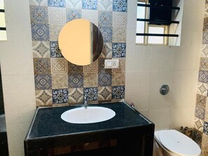 Casa de banho com lavatório, espelho e sanita. A parede está revestida com azulejos estampados.