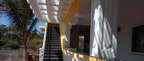 A staircase leading to a building with a yellow and white exterior, surrounded by palm trees and a fenced area.