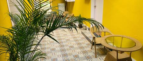 A bright yellow room with patterned floor tiles, a wicker chair, and a small table.