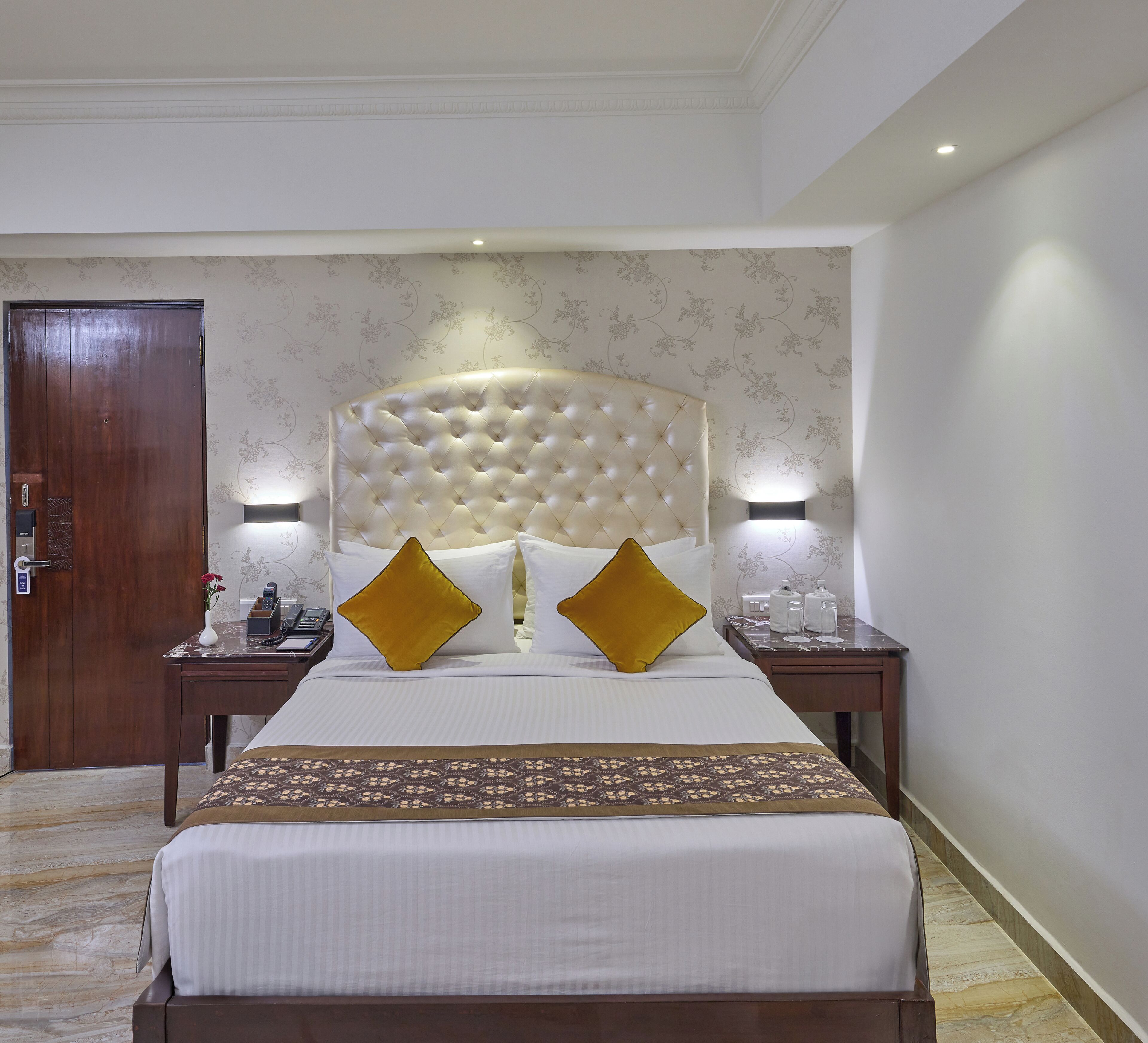 A hotel room with a large bed, two bedside tables, a wooden wardrobe, and a floral wallpaper pattern.