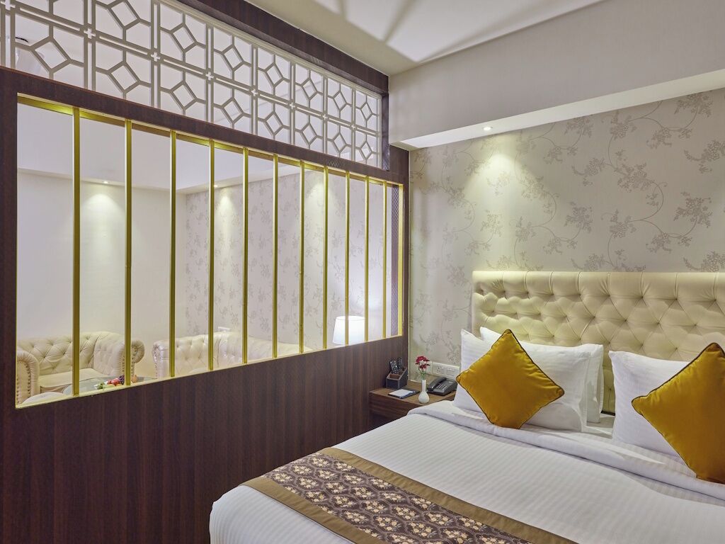 Quarto de hotel com uma cama grande, um painel decorativo na parede, cabeceira estofada e mesa de cabeceira com telefone e vaso.