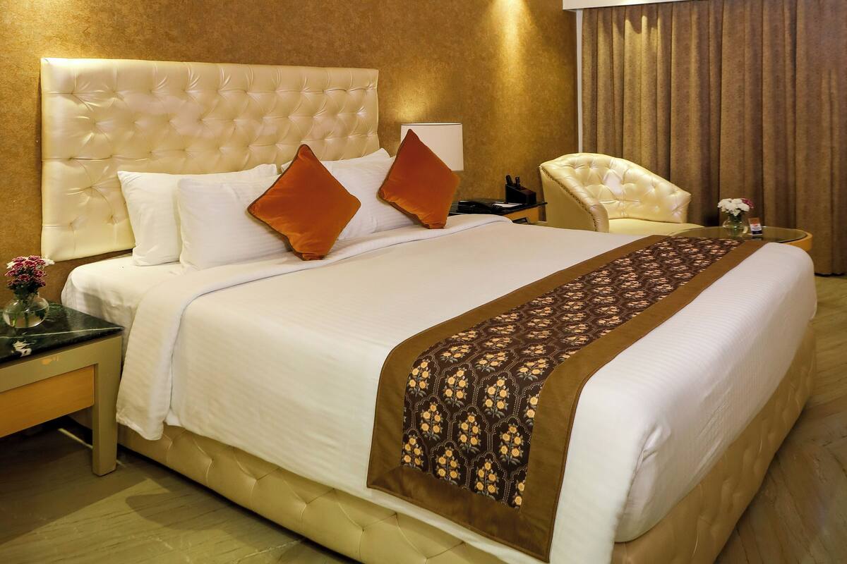 Habitación de hotel con una cama grande, una silla, una mesita de noche, un ventilador de techo y una ventana con cortinas.