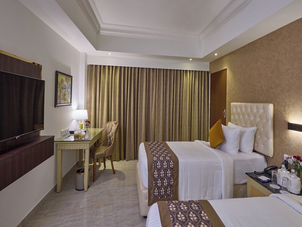Habitación de hotel con dos camas, un escritorio, un televisor y un ventanal grande con cortinas.