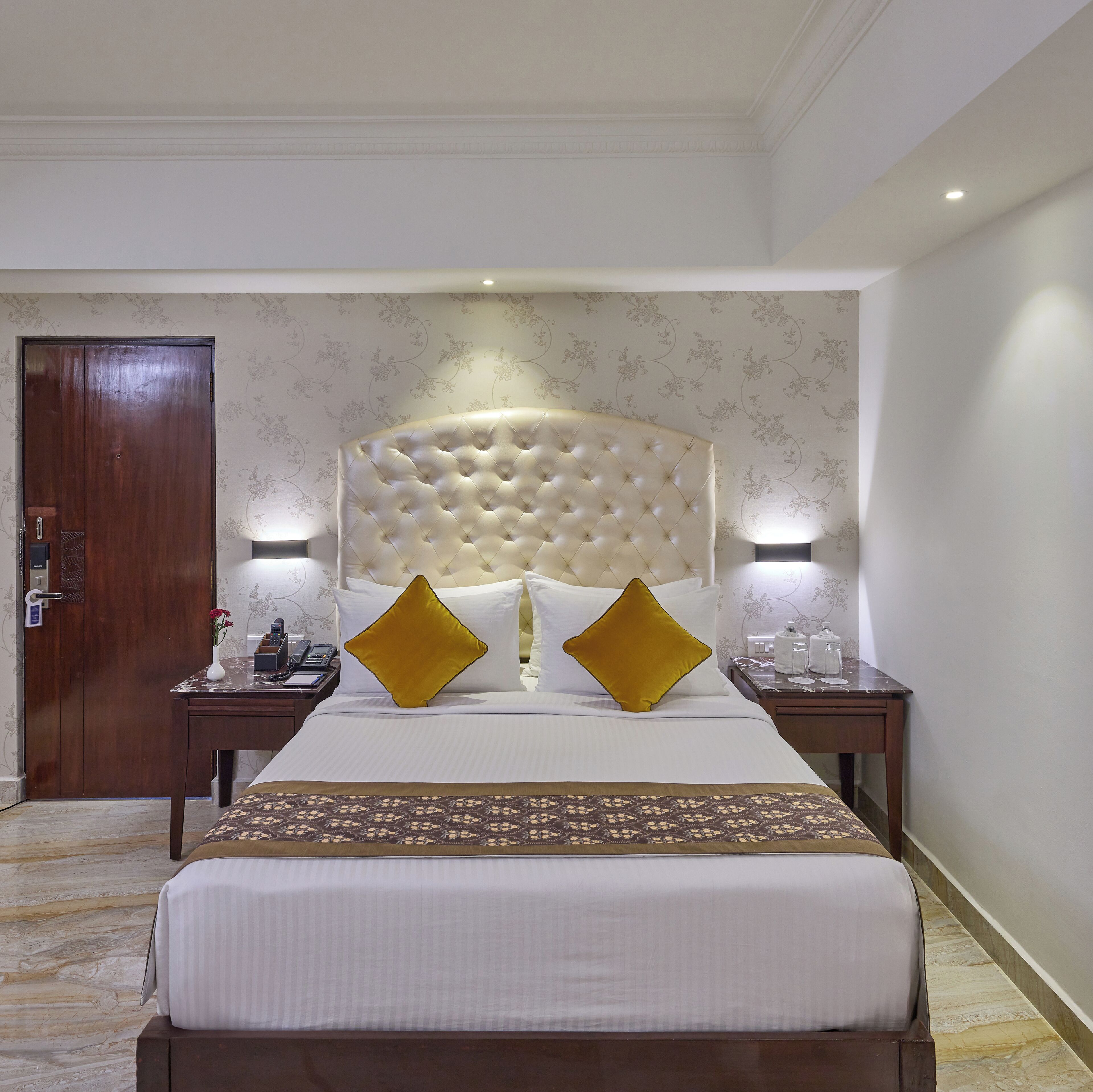Habitación de hotel con una cama grande, dos mesitas de noche, una puerta de madera y un papel tapiz estampado.