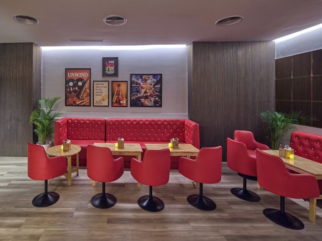 Un comedor moderno con asientos tapizados en rojo, mesas de madera y plantas en macetas.