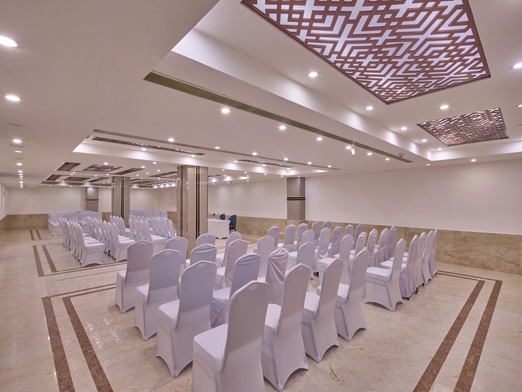 A conference room with rows of tables and chairs, a patterned ceiling design, and a marble floor.