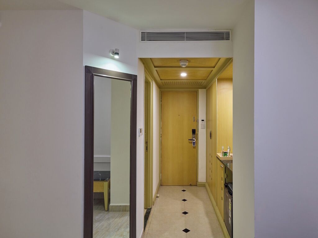 Un couloir étroit, avec une porte en bois au fond, une petite table et une chaise, et un évier sur le mur de droite.