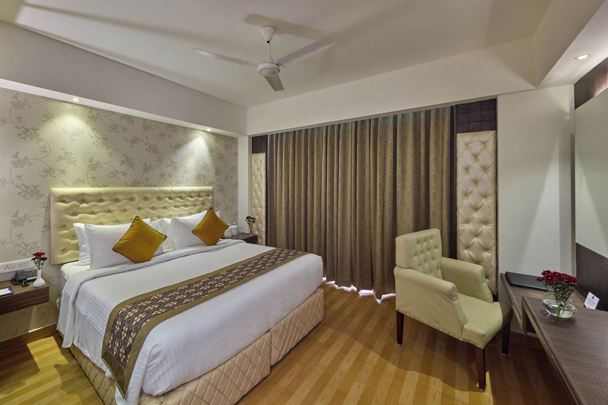 Une chambre d’hôtel avec un grand lit, une chaise, un bureau et un ventilateur de plafond.