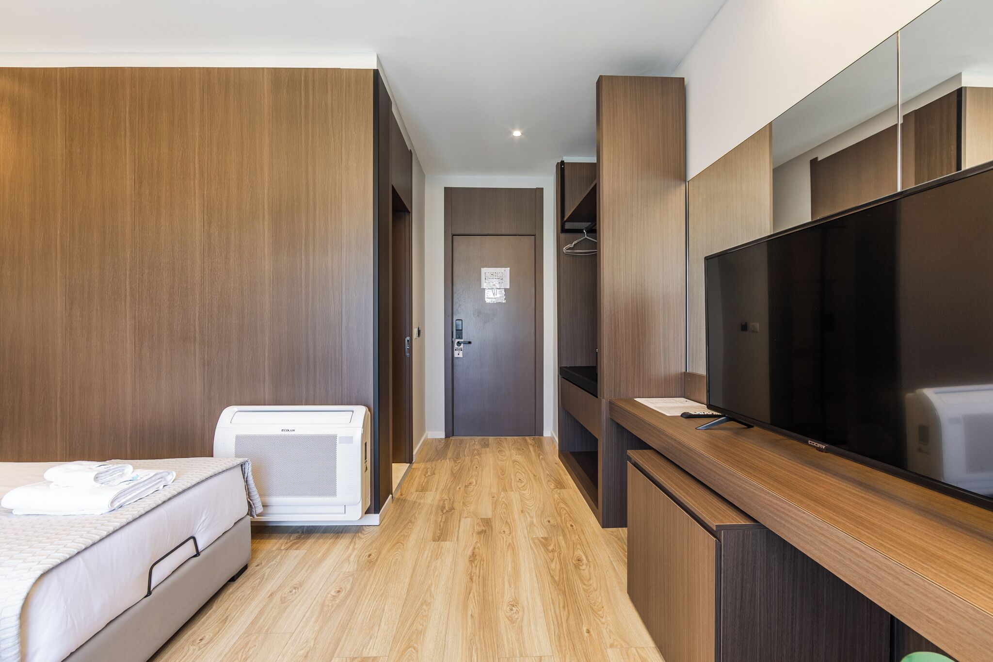 A hotel room with a bed, a TV, a heater, and wooden paneling.