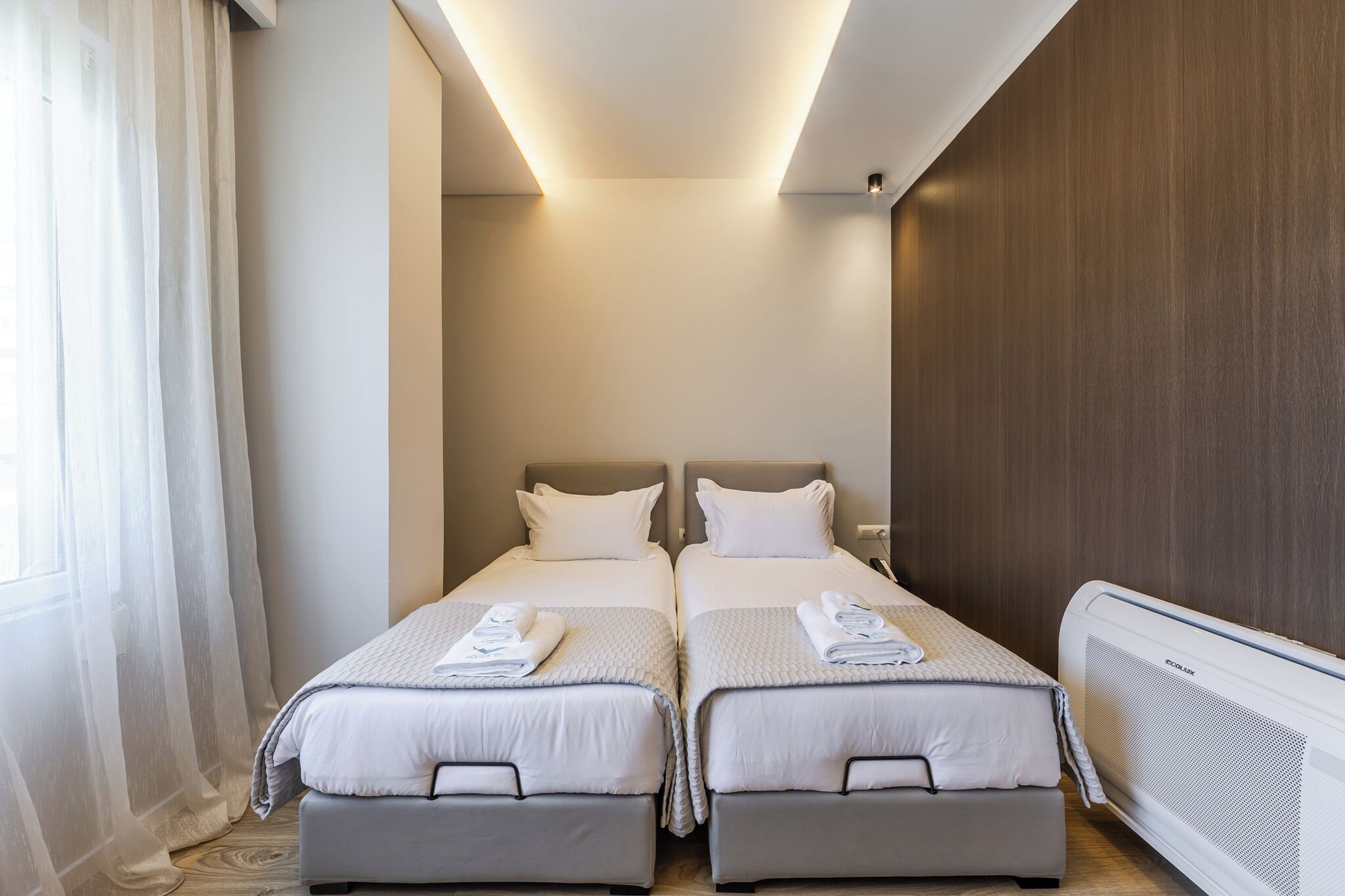 Habitación de hotel con dos camas, una lámpara en el techo, un calentador de pared y cortinas de gasa.