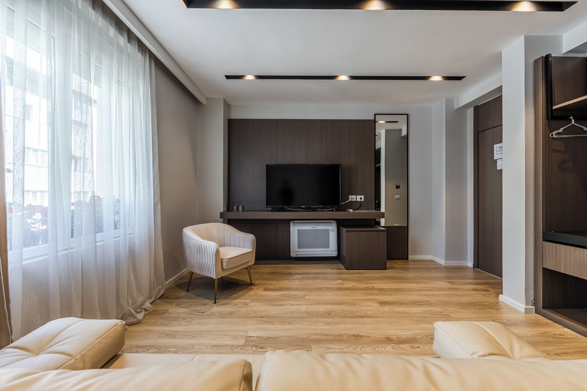 Un salon moderne avec un téléviseur à écran plat, un canapé, un fauteuil et un plancher en bois.