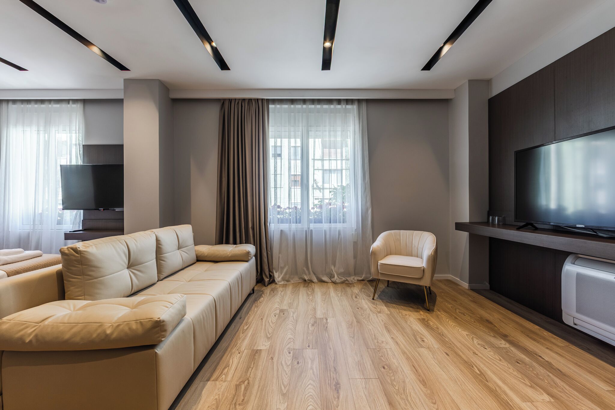 A modern living room with a sectional sofa, a single chair, a flat-screen TV, and a large window with curtains.