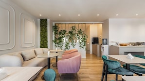 A modern interior with a sofa, chairs, a small table, a kitchen area, and a green wall with plants. - Hotel Aquila D (Durrës)