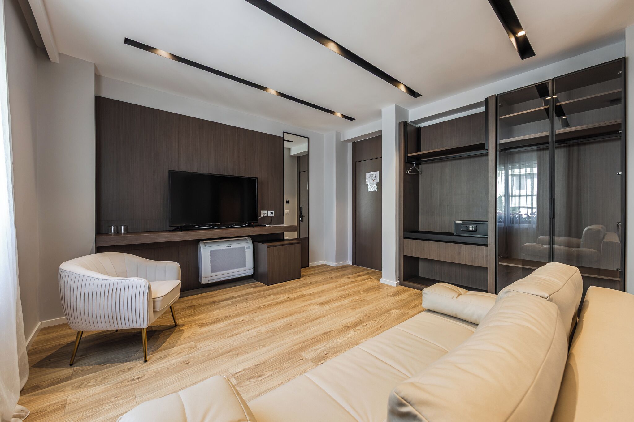 Una sala moderna con un sofá, una silla, un televisor y un área de estar con paredes de vidrio.