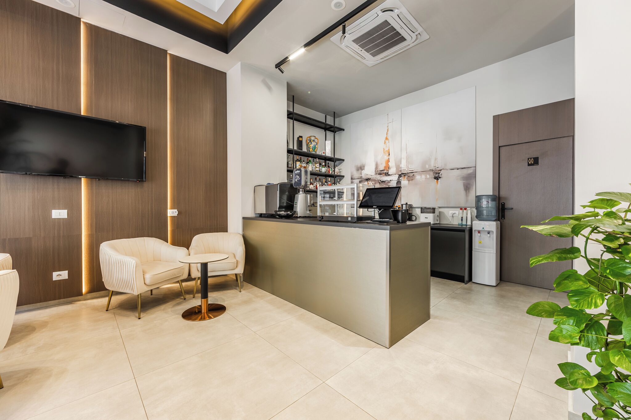 A modern kitchen with a central island, a flat-screen TV mounted on the wall, and a water dispenser.