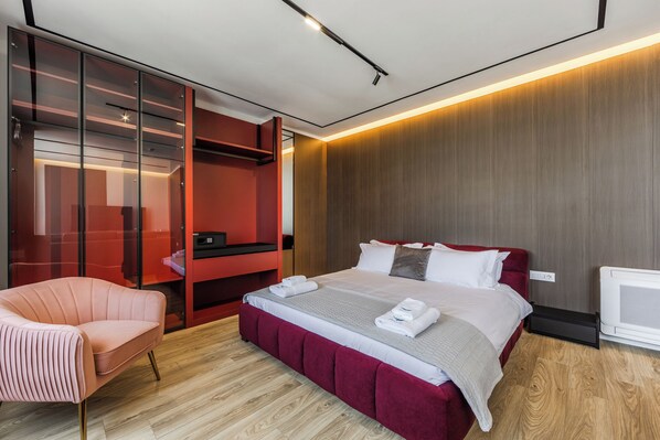 A modern hotel room with a large bed, a red upholstered chair, a glass wardrobe, and a wooden floor. - Hotel Aquila D (Durrës)