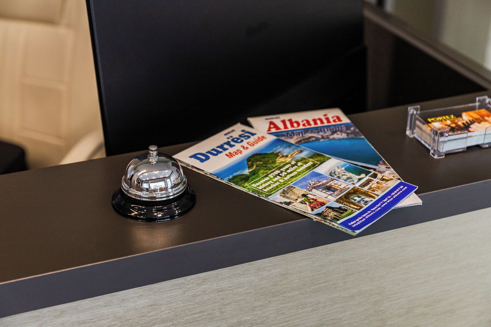 Un mostrador de recepción con un folleto de Albania, una campana de cristal y una vitrina pequeña.