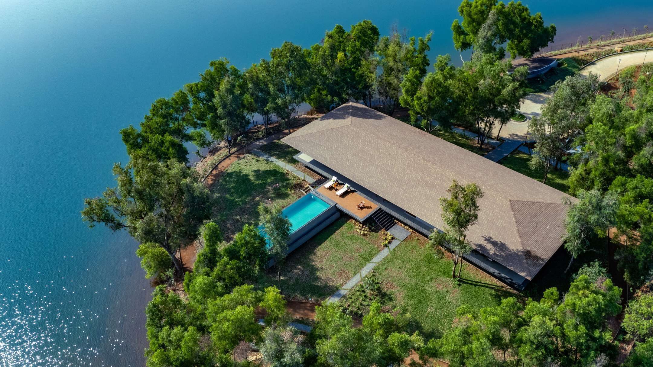 Vista aérea de uma casa moderna com piscina, cercada por vegetação exuberante e uma vista desobstruída do mar.