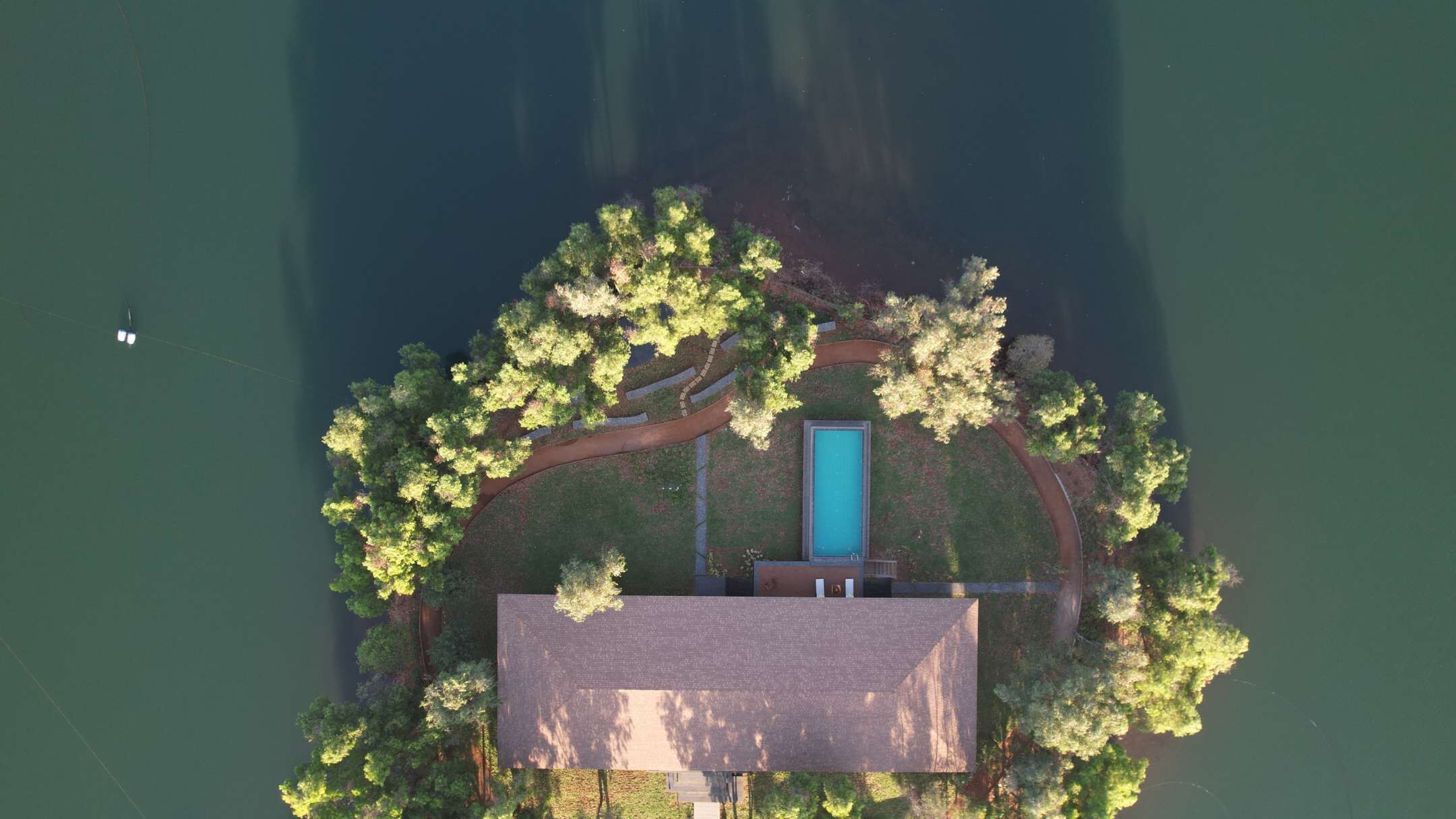 An aerial view of a secluded house with a swimming pool, surrounded by dense trees and a small dock.