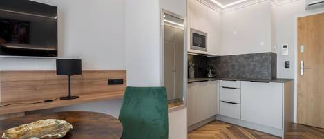 A modern kitchen with white cabinets, a microwave, and a built-in oven. There's a wooden dining table with a green chair and a decorative plate.