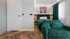 Une chambre moderne avec un canapé vert, un lit recouvert de linge de lit blanc, un tableau abstrait aux couleurs vives et un plancher en bois.