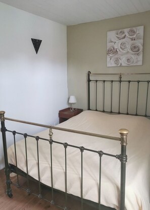 A bedroom with a metal bed frame, a bedside table with a lamp, and a wall-mounted artwork of roses.