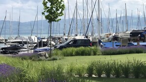 A marina with boats, a car, and a grassy area with purple flowers. - Holiday Apartment Seemöwe with Conservatory, Balcony and Wi-Fi (Kressbronn am Bodensee)