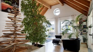 A modern interior with a wooden ceiling, a plant arrangement, a black sofa, and a bookshelf. - Holiday Apartment Seemöwe with Conservatory, Balcony and Wi-Fi (Kressbronn am Bodensee)