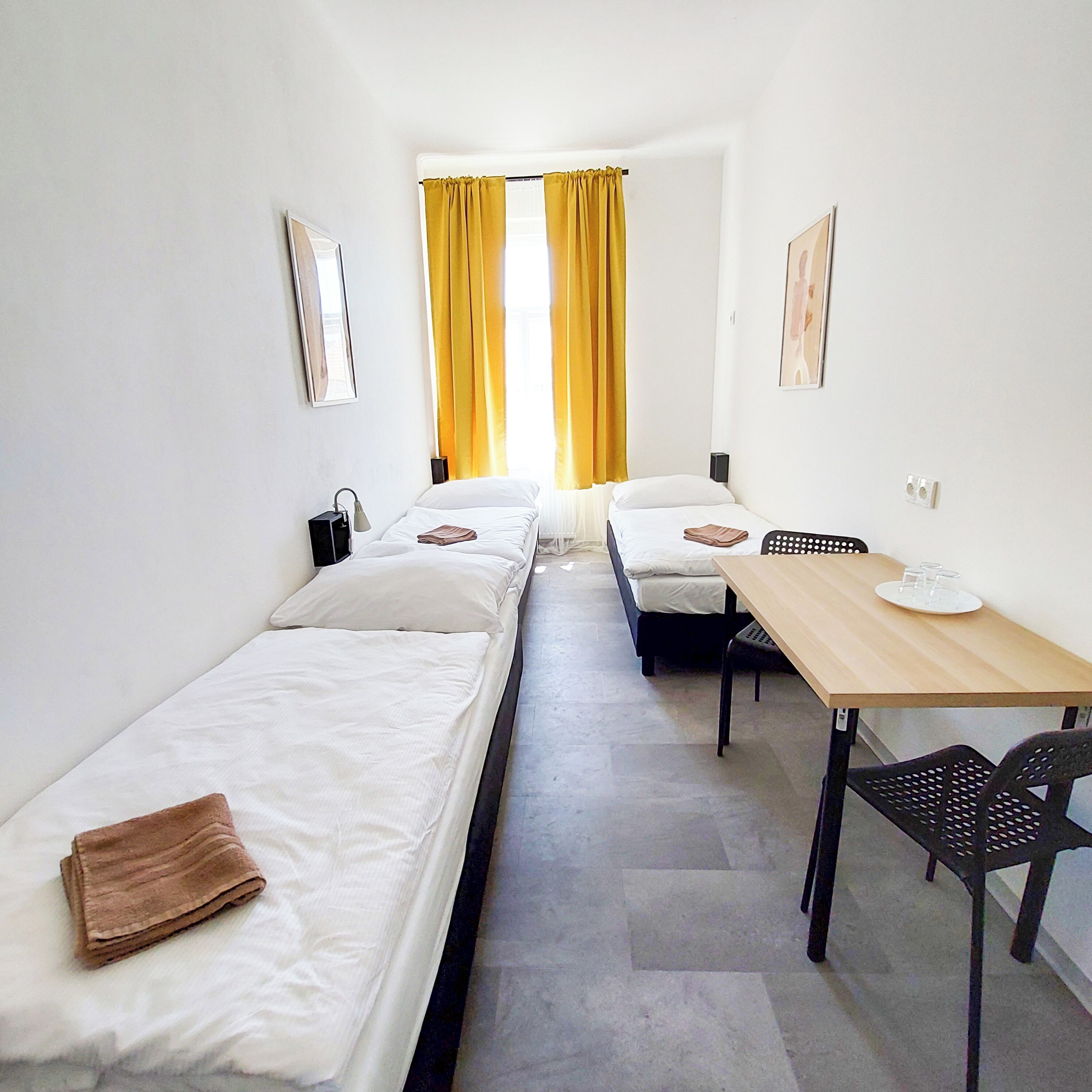 A small, clean room with two single beds, a wooden table, and a chair.