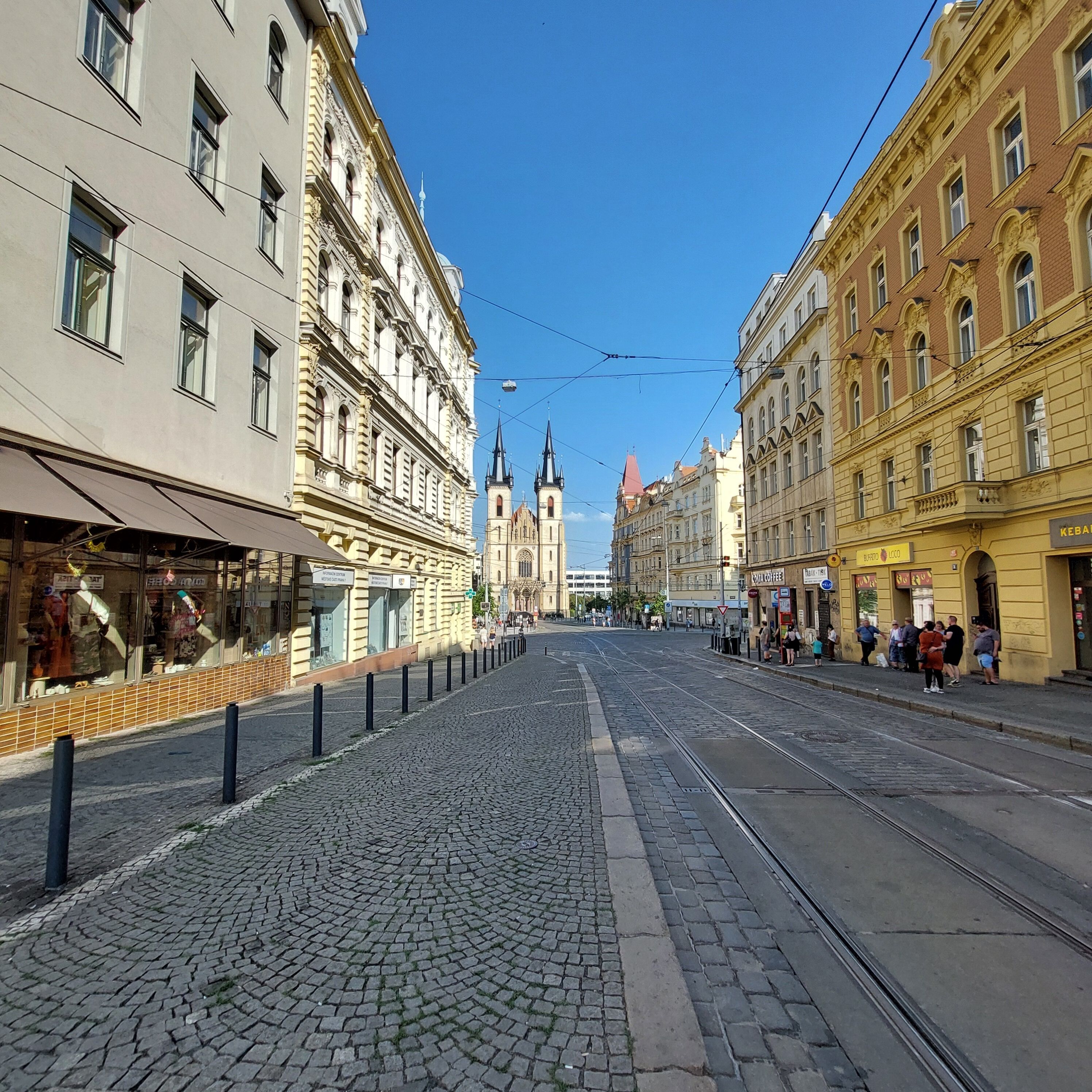 A cobblestone street with historic buildings, a tram line, and a church in the background.